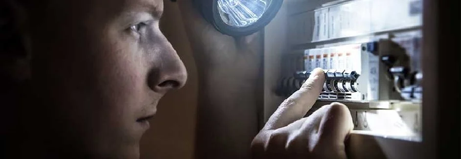 Person mit Taschenlampe am Sicherungskasten